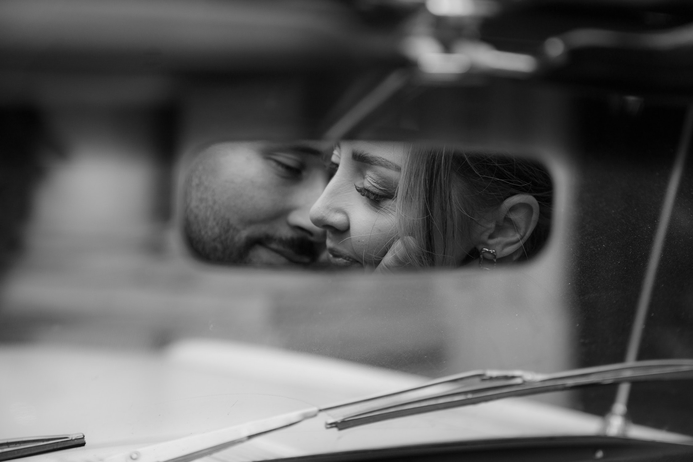Schwarz-Weiß-Detailaufnahme eines Paares im Rückspiegel, natürliche Hochzeitsfotografie, die Emotionen einfängt.